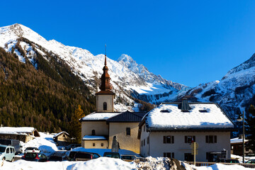 View of bell tower of Saint Pierre Church in center of small village of Argentiere, popular ski and mountaineering resort on background of picturesque snow-capped French Alps on sunny winter day.
