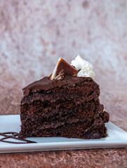 A slice of chocolate cake topped with chocolate fudge frosting and a garnish of chocolate 