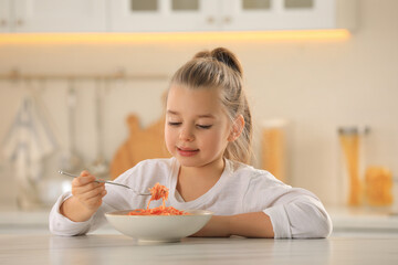 Cute little girl eating tasty pasta at table in kitchen