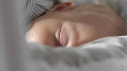 Extreme close up of newborn baby’s face, gently rocking in cot while asleep.