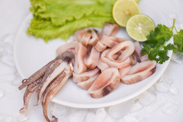 Fresh raw squid with lettuce vegetable salad seafood coriander lemon lime on white plate background, squid rings on ice