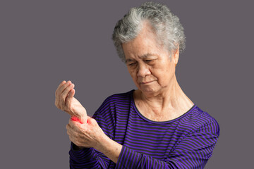 Elderly Asian woman suffering from wrist pain while standing against a gray background.