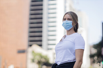 Portrait of a beautiful blonde woman wearing a medical protective mask on his face on a big city street on an urban background. High quality photo