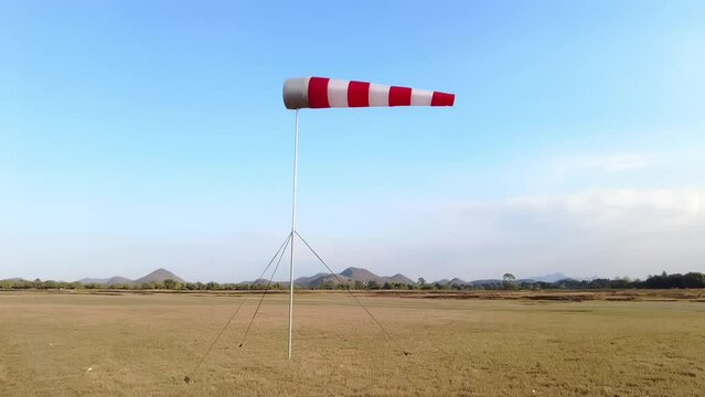 A torn red and white wind sock on a blue sky with clouds at an abandoned airfield.