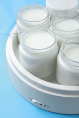 Modern yogurt maker with full jars on light blue background, closeup