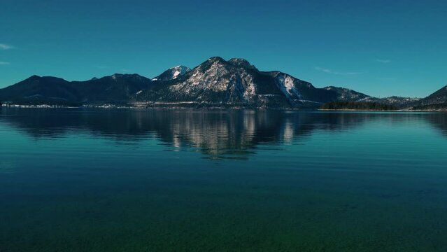 Scenic Bavarian lake Walchensee in south Germany in the alps mountains close to Austria. Blue clear water waves and idyllic blue sky in winter. Seamless video loop cinemagraph 4K UHD aerial drone.
