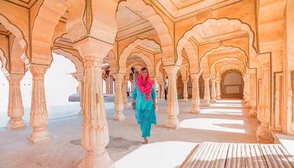 An Indian woman dressed in traditional costume walks between columns - Columned hall of Amber fort - Jaipur, Rajasthan, India - obrazy, fototapety, plakaty