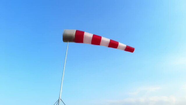 A torn red and white wind sock on a blue sky with clouds at an abandoned airfield