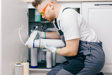 Plumber working change cartridge filter for water in white kitchen. Concept filtration system