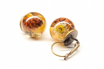 Dried flower resin earrings closeup. Natural plants inside transparent sphere balls, brozen colored base. Selective focus on the details, object isolated on white background.