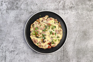 Omelet with sausage and mushrooms on a round plate on a dark gray background. Top view, flat lay