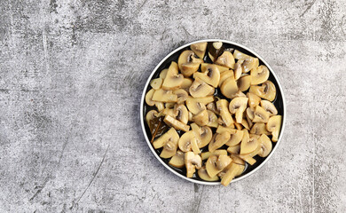 Pickled champignons mushrooms on a round plate on a dark gray background. Top view, flat lay