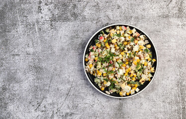 Surimi crab sticks salad with corn, cucumber and seaweed on a round plate on a dark gray background. Top view, flat lay