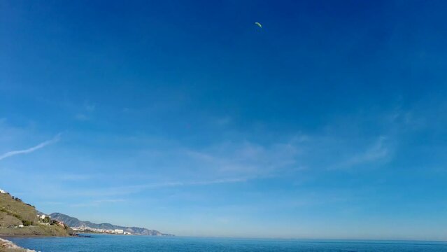 A paramotor flying above the shore outside Nerja. Looking up at a paramotor in the sky. Clear blue sky on the Andalusian coastline in the south part of Spain. Mediterranean coast outside Nerja.