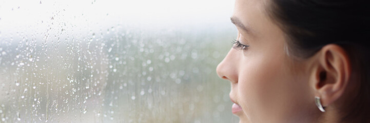 Young pensive woman looking out window at rain