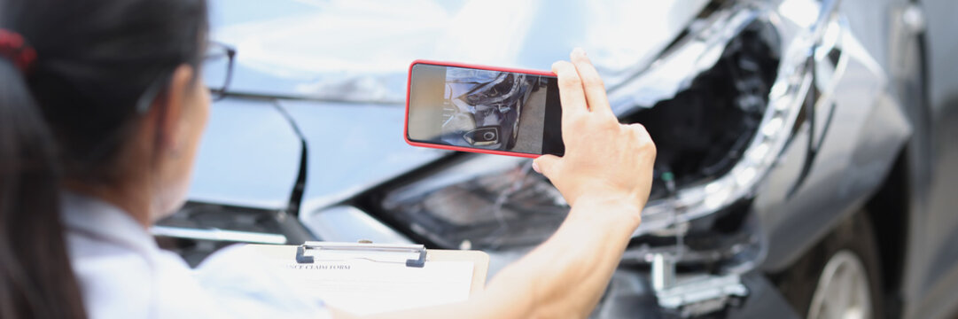 Woman insurance agent taking pictures of broken car on mobile phone closeup