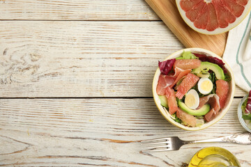 Delicious pomelo salad with prosciutto in half of fruit on white wooden table, flat lay. Space for text