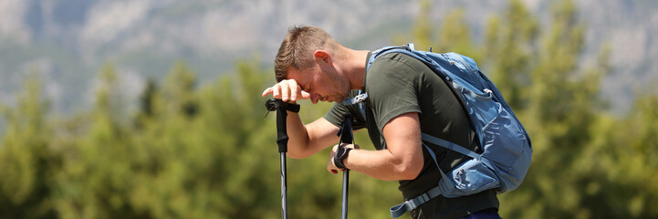 Tired man traveler putting his head on walking sticks against backdrop of mountains