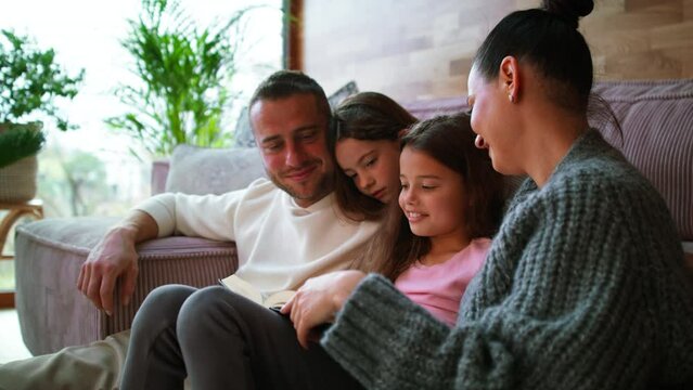 Young family with two little children sitting on floor and reading book at home.