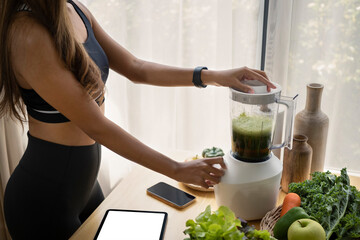 Young woman making fresh organic smoothie with blender in the kitchen.