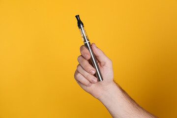 Man holding electronic cigarette on yellow background, closeup
