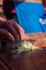 manos cortando cebolla con cuchillo sobre tabla de madera.

cortando ingredientes.

cortando.