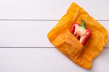 Half of bell pepper in beeswax food wrap on white wooden table, top view. Space for text