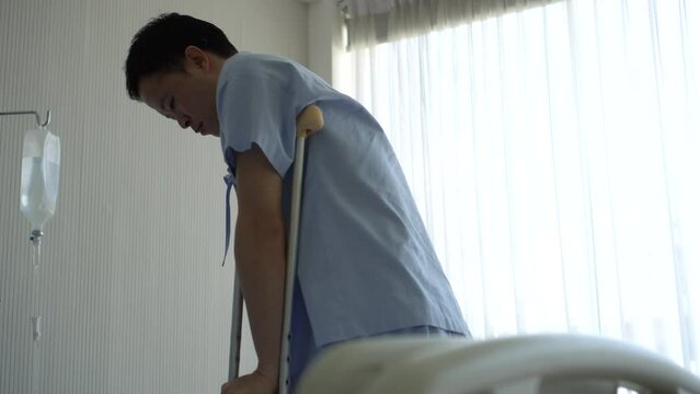 Asian young man use cruthces to walk and sit on hospital bed injure from work accident
