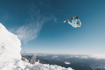 Snowboarder making high flip big air jump in clear blue sunny sky above mountains - obrazy, fototapety, plakaty