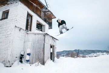 Naklejka premium Snowboarder jumping with grab from abandoned building. Street snowboarding style