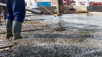 Builders workers pour concrete floor in industrial workshop. Legs in boots in concrete. Submission of concrete for pouring the floor. Monolithic concrete works.