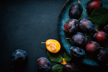 Flat lay composition with fruits on the textured black table surface. Ripe juicy plums with leaves...