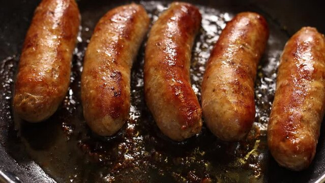 Top close up view of sausages cooking in skillet with steam coming out and oil popping in slow motion. Prepare meat based dinner or launch, dark mood.