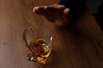Man refusing to drink whiskey at wooden table, closeup. Alcohol addiction treatment