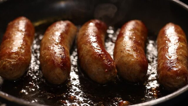 Close up shot of mild italian sausages cooking in skillet. Slow motion of sausage with steam and oil popping in pan. Meat dinner being cooked