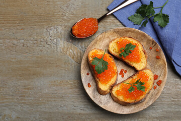 Delicious red caviar sandwiches with parsley on wooden table, flat lay. Space for text