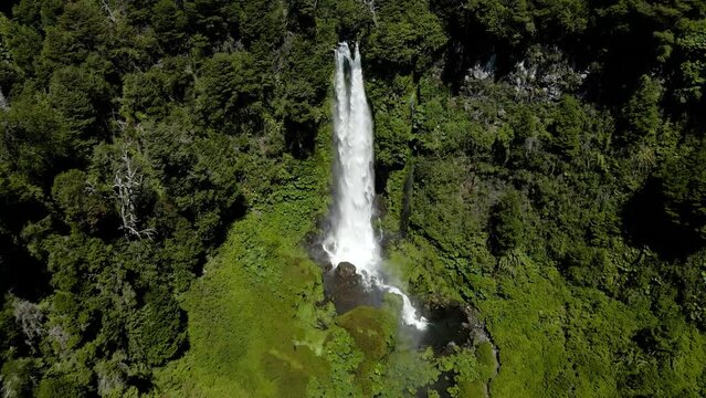 Aerial dolly out of Salto El Leon waterfall streaming on natural pool surrounded by green dense forest, near Pucon, Chile