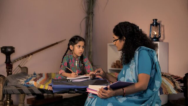 A tuition teacher helping a sweet village school girl to complete her homework -tuition center  village home. An adorable little kid studying while sitting on a Chaarpai - home education  Shiksha  ...