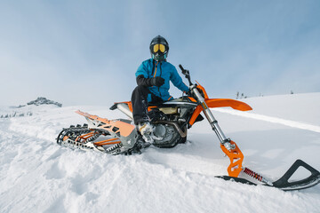 Snowbike rider in mountain valley in beautiful snow powder. Modify dirt bike with snow splashes and trail. Snowmobile sport riding, winter sunny day