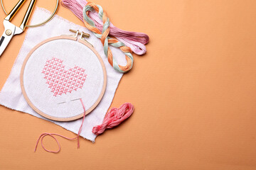 Flat lay composition with embroidery and different sewing accessories on orange background. Space for text