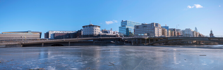 Panorama view, offices, hotels and the central station at the canal Karlbergskanalen with ice floats and an arched walk path and the traffic route Karlbergsleden,  Stockholm