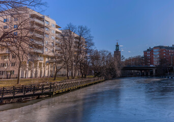 View over the canal Karlbergskanalen with apartment houses and long jetty and skyline with tower of Town City Hall a winter day in Stockholm