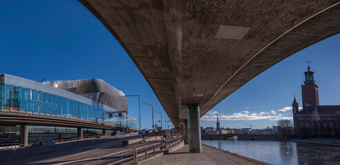 Walk way under a traffic route at the canal Karlbergskanalen, dividing modern buildings from old classic houses with the Town City Hall at the bridge Stadshusbron a sunny winter day in Stockholm