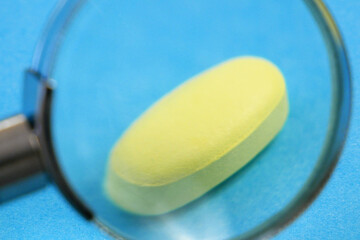 magnifying glass and pill on blue background. checking ingredients and effectiveness of medicine. fake pills concept