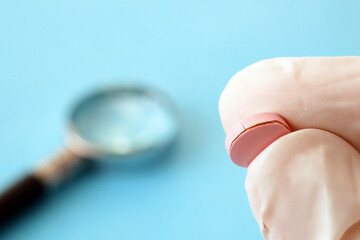 Fototapeta premium magnifying glass and pill on blue background. checking ingredients and effectiveness of medicine. fake pills concept
