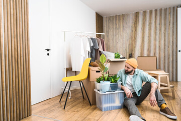 A mature man sitting in unfurnished house, looking at plant in a box. A moving in new home concept.