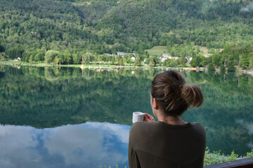 unrecognizable woman drinking coffee in front of the lake of her rural accommodation