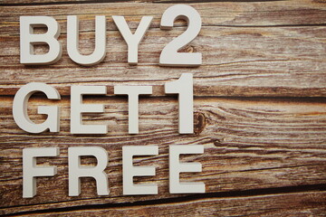 Buy 2 Get 1 Free alphabet letters on wooden background