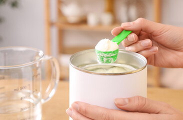 Woman preparing infant formula at table indoors, closeup. Baby milk