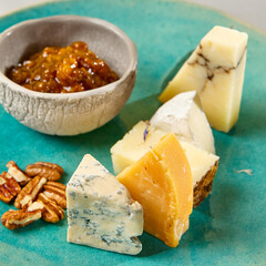 Cheese platter on blue ceramic plate. Cheeseboard on handmade dinner plate in modern style. Different cheese on ceramic dishware in minimal style.
